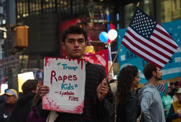 October 18, 2025, New York, New York, USA: A protester holds an American flag and a sign that reads, Ã¢â‚¬oeTrump Rapes Kids - Epstein FilesÃ¢â‚¬Â at the New York City No Kings protest. New York USA - ZUMAl171 20251018_znp_l171_039 Copyright: xEdnaxLeshowitzx