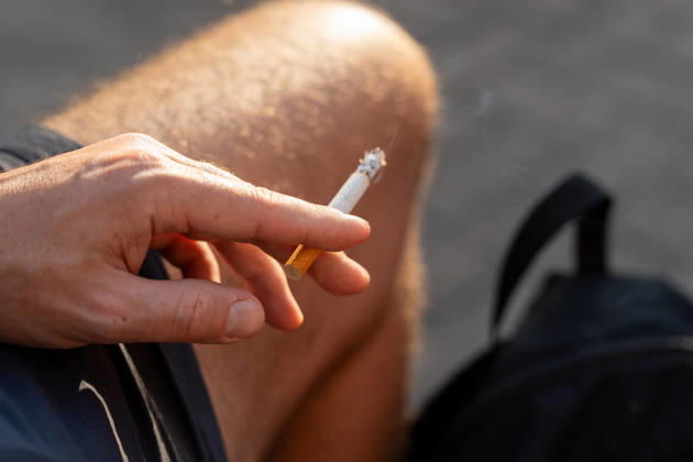 Basseterre, St. Kitts, St. Kitts and Nevis - January 9, 2026: A man smokes a cigarette in swimming trunks outdoors. Smoking is considered a harmful stimulant and poses risks due to nicotine consumption and tobacco smoke. Symbolic image for smoking and addiction