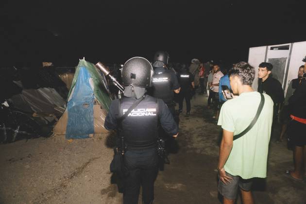 October 3, 2026, Ceuta, Ceuta, Spain: A riot police officer stands among young men and tents at a makeshift migrant camp in Ceuta at night. Riot police escorted firefighters through the camp on the night of October 3 to put out the fires that people living there use to cook their food. Thousands of migrants, most of them young Moroccan men, have been living in makeshift settlements in the Spanish North African enclave of Ceuta since a mass arrival at the end of July 2026 set off a migration and political crisis. Ceuta Spain - ZUMAs392 20261003_zip_s392_016 Copyright: xFabianxSuspensivox