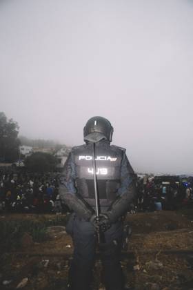 October 4, 2026, Ceuta, Ceuta, Spain: A riot police officer stands guard in the fog in front of migrants sitting on the ground during the eviction of the makeshift camp on El Trampolin beach in Ceuta. Spanish National Police began evicting the makeshift camp on El Trampolin beach in Ceuta on October 4, where more than 3,000 migrants, most of them young Moroccan men, were living. Dozens of police vans, armoured vehicles of the Police Intervention Units (UIP), drones and boats took part in the operation. People were taken by bus to the temporary centre at the Tarajal border to be identified, and the authorities plan to clear the beach in phases before October 15. The camp grew after a mass arrival at the end of July 2026 set off a migration a - ZUMAs392 20261004_zip_s392_002 Copyright: xFabianxSuspensivox