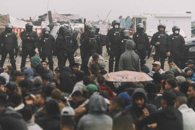 October 4, 2026, Ceuta, Ceuta, Spain: Riot police officers stand in front of hundreds of migrants sitting on the ground during the eviction of the makeshift camp on El Trampolin beach in Ceuta. Spanish National Police began evicting the makeshift camp on El Trampolin beach in Ceuta on October 4, where more than 3,000 migrants, most of them young Moroccan men, were living. Dozens of police vans, armoured vehicles of the Police Intervention Units (UIP), drones and boats took part in the operation. People were taken by bus to the temporary centre at the Tarajal border to be identified, and the authorities plan to clear the beach in phases before October 15. The camp grew after a mass arrival at the end of July 2026 set off a migration and poli - ZUMAs392 20261004_zip_s392_007 Copyright: xFabianxSuspensivox