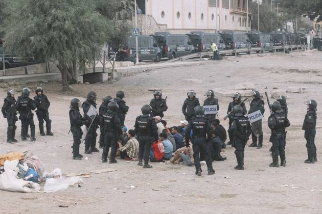 October 4, 2026, Ceuta, Ceuta, Spain: Riot police officers surround a group of migrants sitting on the ground, with a line of police vans behind, during the eviction of the makeshift camp on El Trampolin beach in Ceuta. Spanish National Police began evicting the makeshift camp on El Trampolin beach in Ceuta on October 4, where more than 3,000 migrants, most of them young Moroccan men, were living. Dozens of police vans, armoured vehicles of the Police Intervention Units (UIP), drones and boats took part in the operation. People were taken by bus to the temporary centre at the Tarajal border to be identified, and the authorities plan to clear the beach in phases before October 15. The camp grew after a mass arrival at the end of July 2026 se - ZUMAs392 20261004_zip_s392_043 Copyright: xFabianxSuspensivox