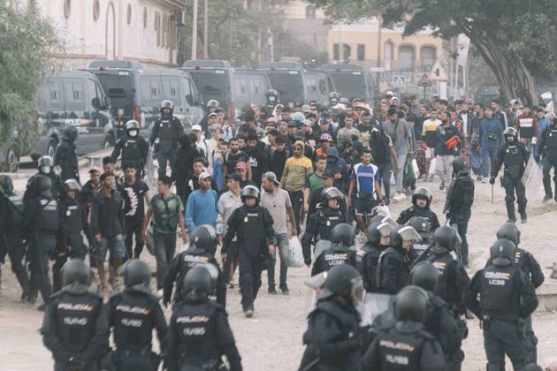 October 4, 2026, Ceuta, Ceuta, Spain: Dozens of young migrants walk escorted by riot police officers during the eviction of the makeshift camp on El Trampolin beach in Ceuta. Spanish National Police began evicting the makeshift camp on El Trampolin beach in Ceuta on October 4, where more than 3,000 migrants, most of them young Moroccan men, were living. Dozens of police vans, armoured vehicles of the Police Intervention Units (UIP), drones and boats took part in the operation. People were taken by bus to the temporary centre at the Tarajal border to be identified, and the authorities plan to clear the beach in phases before October 15. The camp grew after a mass arrival at the end of July 2026 set off a migration and political crisis. Ceut - ZUMAs392 20261004_zip_s392_044 Copyright: xFabianxSuspensivox