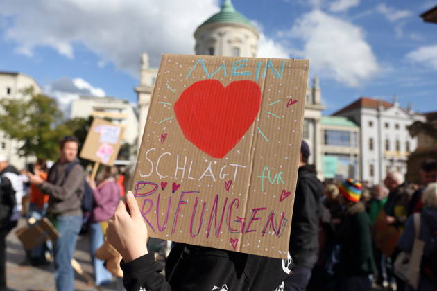A protester stands in the Alter Markt holding a sign that reads My Heart Beats for Exams during a demonstration calling for the Federal Constitutional Court to review far-right parties, Potsdam, October 10, 2026. Protest demonstration in Potsdam