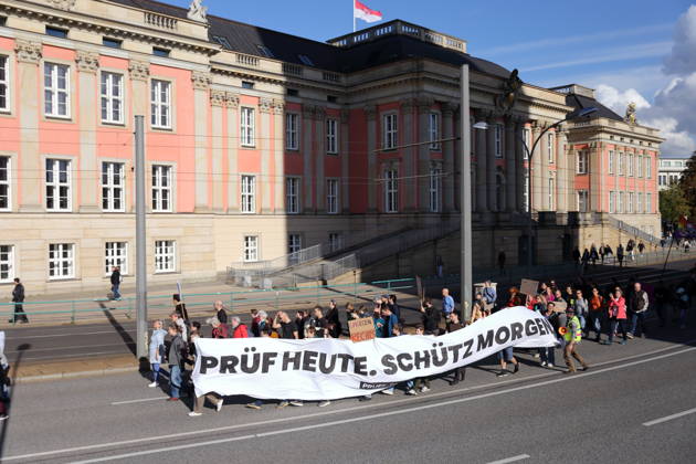 Protesters march with a banner reading Review today, Schütz tomorrow at the state parliament during a demonstration calling for the Federal Constitutional Court to review far-right parties, Potsdam, October 10, 2026. Review demonstration in Potsdam