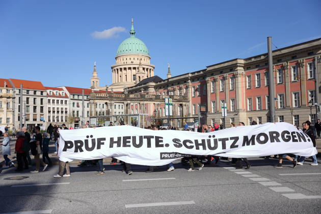 Protesters march with a banner reading Review today, Schütz tomorrow at the state parliament during a demonstration calling for the Federal Constitutional Court to review far-right parties, Potsdam, October 10, 2026. Review demonstration in Potsdam