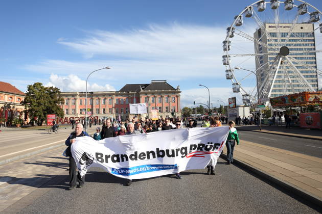 Protesters walk down Breite Straße carrying a banner reading Brandenburg: Investigate during a demonstration calling for the Federal Constitutional Court to review far-right parties, Potsdam, October 10, 2026. Investigate demonstration in Potsdam