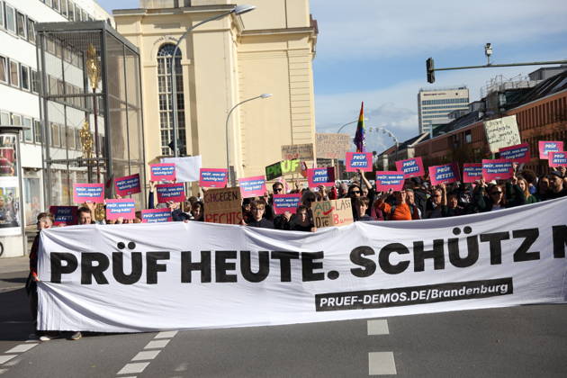 Protesters stand on Breite Straße holding a banner reading Review Today, Ban Tomorrow during a demonstration calling for the Federal Constitutional Court to review far-right parties, Potsdam, October 10, 2026. Review Demonstration in Potsdam