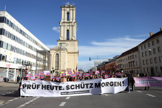 Protesters stand on Breite Straße holding a banner reading Review Today, Ban Tomorrow during a demonstration calling for the Federal Constitutional Court to review far-right parties, Potsdam, October 10, 2026. Review Demonstration in Potsdam