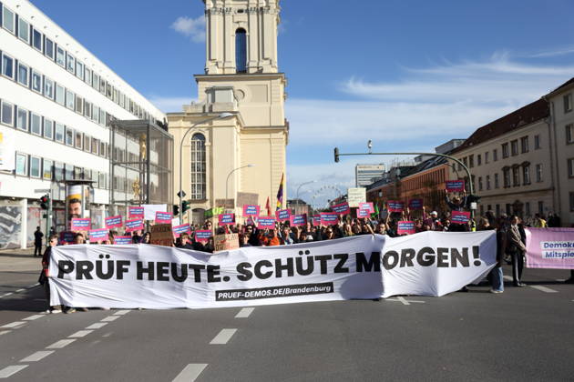 Protesters stand on Breite Straße holding a banner reading Review Today, Ban Tomorrow during a demonstration calling for the Federal Constitutional Court to review far-right parties, Potsdam, October 10, 2026. Review Demonstration in Potsdam