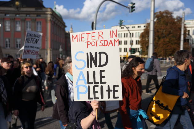 A protester walks across the Lange Brücke in Potsdam carrying a sign that reads Tenants: Are We All Broke? during a demonstration against the housing crisis and rising rents, Potsdam, October 10, 2026. Rent Protest in Potsdam