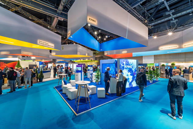 Berlin, 13.10.2026: Besucher am Messestand von KPMG auf der Smart Country Convention in der Halle hub27, links die Deckenaufbauten von Controlware sowie Rohde & Schwarz Networks and Cybersecurity, rechts mgm technology partners. Beratungsunternehmen wie KPMG begleiten Bund, Länder und Kommunen bei der Digitalisierung ihrer Verwaltungsprozesse. Die Smart Country Convention (SCCON) ist die Kongressmesse für die Digitalisierung des öffentlichen Sektors und wird vom Digitalverband Bitkom gemeinsam mit der Messe Berlin veranstaltet. Vom 13. bis 15. Oktober 2026 treffen sich in der Halle hub27 Vertreter aus Bund, Ländern und Kommunen mit Unternehmen der Digitalwirtschaft, um über digitale Verwaltung, Smart City und digitale Souveränität zu