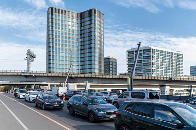 Berlin, 13.10.2026: Dichter Autoverkehr vor einer Bahnbrücke: Das Hochhaus des neuen DKB-Campus prägt den nördlichen Teil der Europacity in Berlin-Mitte, rechts weitere Neubauten des Stadtquartiers. Die Deutsche Kreditbank AG (DKB) hat ihren neuen Hauptsitz heute offiziell eröffnet. Der von Kleihues + Kleihues entworfene, rund 82 Meter hohe Komplex besteht aus drei Gebäudeteilen mit fünf, elf und 19 Geschossen und rund 35.000 Quadratmetern Mietfläche; entwickelt wurde er von der CA Immo unter dem Projektnamen Upbeat. Rund 2.600 Mitarbeitende des DKB-Konzerns, die bislang auf mehrere Berliner Standorte verteilt waren, arbeiten nun gemeinsam im Campus. Die DKB ist Exklusivmieterin und hat einen Mietvertrag über 15 Jahre abgeschl