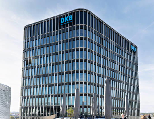 Berlin, 13.10.2026: Das Gebäude des neuen DKB-Campus in der Europacity in Berlin-Mitte mit dem Schriftzug DKB Deutsche Kreditbank AG, im Vordergrund eine Dachterrasse mit zusammengeklappten Sonnenschirmen. Die Deutsche Kreditbank AG (DKB) hat ihren neuen Hauptsitz heute offiziell eröffnet. Der von Kleihues + Kleihues entworfene, rund 82 Meter hohe Komplex besteht aus drei Gebäudeteilen mit fünf, elf und 19 Geschossen und rund 35.000 Quadratmetern Mietfläche; entwickelt wurde er von der CA Immo unter dem Projektnamen Upbeat. Rund 2.600 Mitarbeitende des DKB-Konzerns, die bislang auf mehrere Berliner Standorte verteilt waren, arbeiten nun gemeinsam im Campus. Die DKB ist Exklusivmieterin und hat einen Mietvertrag über 15 Jah