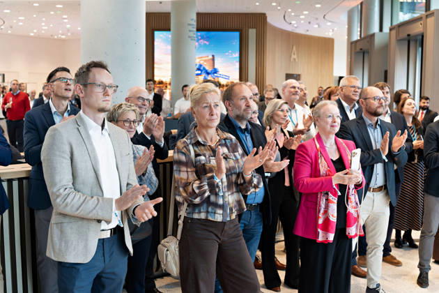 Berlin, 13.10.2026: Gäste applaudieren bei der Eröffnungsfeier im Foyer des neuen DKB-Campus in der Europacity in Berlin-Mitte; im Hintergrund zeigt ein Bildschirm das Motiv der Eröffnungswoche. Die Deutsche Kreditbank AG (DKB) hat ihren neuen Hauptsitz heute offiziell eröffnet. Der von Kleihues + Kleihues entworfene, rund 82 Meter hohe Komplex besteht aus drei Gebäudeteilen mit fünf, elf und 19 Geschossen und rund 35.000 Quadratmetern Mietfläche; entwickelt wurde er von der CA Immo unter dem Projektnamen Upbeat. Rund 2.600 Mitarbeitende des DKB-Konzerns, die bislang auf mehrere Berliner Standorte verteilt waren, arbeiten nun gemeinsam im Campus. Die DKB ist Exklusivmieterin und hat einen Mietvertrag über 15 Jahre abgeschlosse