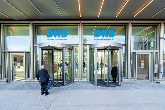 Berlin, 13.10.2026: Besucher gehen durch die Drehtüren am Eingang des neuen DKB-Campus in der Europacity in Berlin-Mitte, darüber der Schriftzug DKB Deutsche Kreditbank AG. Die Deutsche Kreditbank AG (DKB) hat ihren neuen Hauptsitz heute offiziell eröffnet. Der von Kleihues + Kleihues entworfene, rund 82 Meter hohe Komplex besteht aus drei Gebäudeteilen mit fünf, elf und 19 Geschossen und rund 35.000 Quadratmetern Mietfläche; entwickelt wurde er von der CA Immo unter dem Projektnamen Upbeat. Rund 2.600 Mitarbeitende des DKB-Konzerns, die bislang auf mehrere Berliner Standorte verteilt waren, arbeiten nun gemeinsam im Campus. Die DKB ist Exklusivmieterin und hat einen Mietvertrag über 15 Jahre abgeschlossen. DKB eröffnet