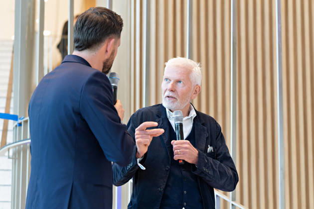 Berlin, 13.10.2026: Ein Moderator (l.) im Gespräch mit dem Architekten des Gebäudes vom Büro Kleihues + Kleihues (r.) bei der Eröffnungsfeier im Foyer des neuen DKB-Campus in der Europacity in Berlin-Mitte. Die Deutsche Kreditbank AG (DKB) hat ihren neuen Hauptsitz heute offiziell eröffnet. Der von Kleihues + Kleihues entworfene, rund 82 Meter hohe Komplex besteht aus drei Gebäudeteilen mit fünf, elf und 19 Geschossen und rund 35.000 Quadratmetern Mietfläche; entwickelt wurde er von der CA Immo unter dem Projektnamen Upbeat. Rund 2.600 Mitarbeitende des DKB-Konzerns, die bislang auf mehrere Berliner Standorte verteilt waren, arbeiten nun gemeinsam im Campus. Die DKB ist Exklusivmieterin und hat einen Mietvertrag über 15 Jahre