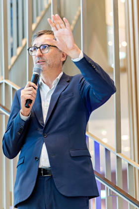 Berlin, 13.10.2026: DKB-CEO Dr. Sven Deglow gestikuliert bei seiner Rede auf der Treppe im Foyer des neuen DKB-Campus in der Europacity in Berlin-Mitte. Die Deutsche Kreditbank AG (DKB) hat ihren neuen Hauptsitz heute offiziell eröffnet. Der von Kleihues + Kleihues entworfene, rund 82 Meter hohe Komplex besteht aus drei Gebäudeteilen mit fünf, elf und 19 Geschossen und rund 35.000 Quadratmetern Mietfläche; entwickelt wurde er von der CA Immo unter dem Projektnamen Upbeat. Rund 2.600 Mitarbeitende des DKB-Konzerns, die bislang auf mehrere Berliner Standorte verteilt waren, arbeiten nun gemeinsam im Campus. Die DKB ist Exklusivmieterin und hat einen Mietvertrag über 15 Jahre abgeschlossen. Die DKB unterstreicht mit dem langfristig