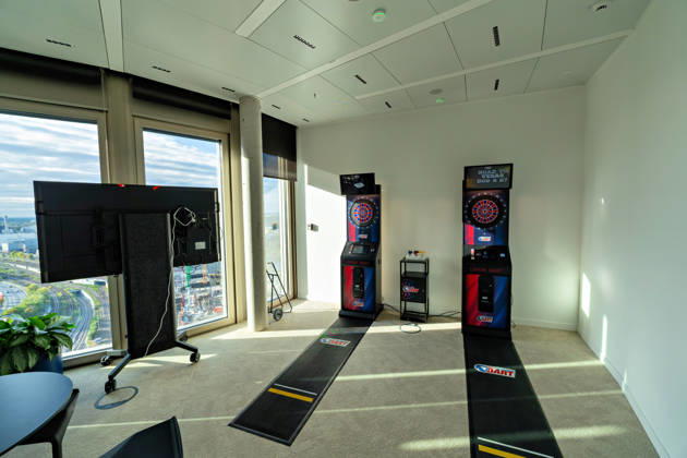 Berlin, 13.10.2026: Ein Spielzimmer mit zwei elektronischen Dartautomaten im neuen DKB-Campus in der Europacity in Berlin-Mitte; durch die Fenster sieht man die Bahngleise. Die Deutsche Kreditbank AG (DKB) hat ihren neuen Hauptsitz heute offiziell eröffnet. Der von Kleihues + Kleihues entworfene, rund 82 Meter hohe Komplex besteht aus drei Gebäudeteilen mit fünf, elf und 19 Geschossen und rund 35.000 Quadratmetern Mietfläche; entwickelt wurde er von der CA Immo unter dem Projektnamen Upbeat. Rund 2.600 Mitarbeitende des DKB-Konzerns, die bislang auf mehrere Berliner Standorte verteilt waren, arbeiten nun gemeinsam im Campus. Die DKB ist Exklusivmieterin und hat einen Mietvertrag über 15 Jahre abgeschlossen. Moderne Arbeits- und K