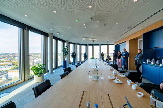Berlin, 13.10.2026: Besucherinnen und Besucher sehen sich am Eröffnungstag einen Konferenzraum mit langer Tafel und Rundumblick über Berlin im neuen DKB-Campus in der Europacity in Berlin-Mitte an. Die Deutsche Kreditbank AG (DKB) hat ihren neuen Hauptsitz heute offiziell eröffnet. Der von Kleihues + Kleihues entworfene, rund 82 Meter hohe Komplex besteht aus drei Gebäudeteilen mit fünf, elf und 19 Geschossen und rund 35.000 Quadratmetern Mietfläche; entwickelt wurde er von der CA Immo unter dem Projektnamen Upbeat. Rund 2.600 Mitarbeitende des DKB-Konzerns, die bislang auf mehrere Berliner Standorte verteilt waren, arbeiten nun gemeinsam im Campus. Die DKB ist Exklusivmieterin und hat einen Mietvertrag über 15 Jahre abgeschlos