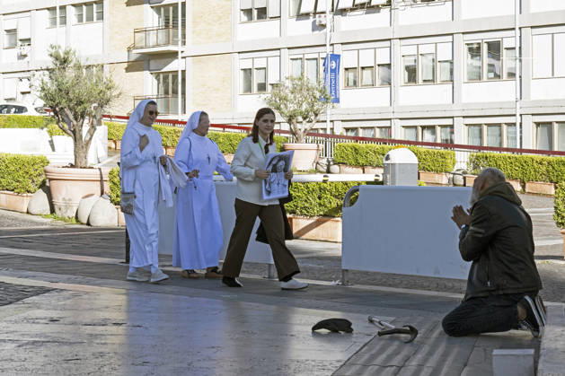 ITALY - POPE - VATICAN-2026 10 15 Italy, Rome, Vatican City, October 15, 2026. A young girl, who drew the picture, accompanied by two nuns, walks past a beggar before placing a portrait of Pope Leo XIV at the foot of the statue of Pope John Paul II, outside the Agostino Gemelli University Hospital, where Pope Leo XIV is hospitalized, in Rome, Italy, on October 15, 2026. According to the Holy See Press Office, Pope Leo XIV is recovering after successfully undergoing surgery on October 13 to remove the lower lobe of his right lung. During the operation, doctors confirmed the diagnosis of lung adenocarcinoma. Photo by ALESSIA GIULIANI Catholic Press Photo EDITORIAL USE ONLY - NO BOOKS Copyright: xALESSIAxGIULIANI xCatholicxPressxPhotox
