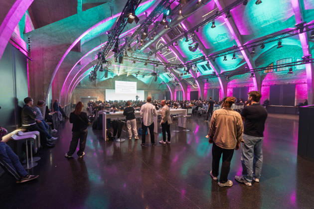 Berlin, 16.10.2026: Teilnehmerinnen und Teilnehmer der NeulandPro Connect 2026 verfolgen in der vollen Halle des WECC stehend und sitzend den Vortrag des Publizisten und Digital-Vordenkers Sascha Lobo. Die zweitägige KI-Konferenz NeulandPro Connect 2026 findet am 16. und 17. Oktober im Westhafen Event & Convention Center (WECC) in Moabit statt, einem historischen Speichergebäude am Berliner Westhafen. Veranstalter ist NeulandPro, eine Bildungs- und Medienmarke rund um Künstliche Intelligenz. Mit Vorträgen, Workshops und Hackathons richtet sich die Konferenz vor allem an kleine und mittelständische Unternehmen, Gründer und Führungskräfte, die KI praktisch einsetzen wollen; erwartet werden bis zu 1.000 Gäste. NeulandPro Connect 2026