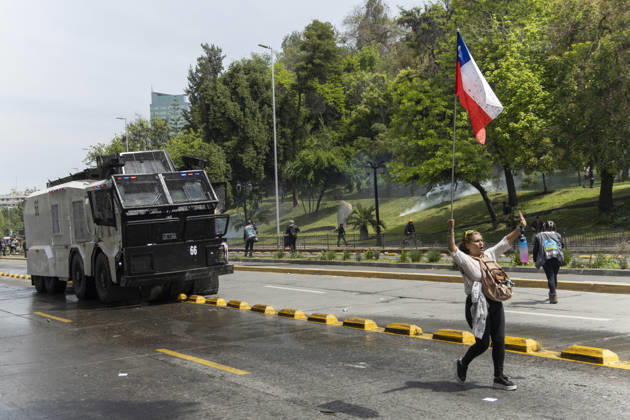 October 19, 2026, Santiago, Chile: A woman walks with a Chilean flag in front of an armored police car. In the center of the capital of Chile, different incidents took place between demonstrators and the police. The riots were carried out during the commemoration of the 7 years after the social outcast that happened on October 18, 2019. Santiago Chile - ZUMAs197 20261019_aaa_s197_016 Copyright: xSebastianxNancox