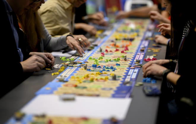 Visitors are playing *The Settlers of Catan* (Kosmos) at a long table, a game table, on October 22, 2026, at the SPIEL Essen trade fair, which runs from October 22 to October 25, 2026, in Essen, Germany, at the Grugahalle.