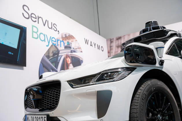 Munich, Bavaria, Germany October 23, 2026: The 2026 convention of the CSU (Christian Social Union) party at the Munich Trade Fair Center. Background image: a close-up of a white Jaguar I-PACE equipped with autonomous driving technology from the U.S. company Waymo. The electric vehicle is equipped with cameras, LiDAR, and radar sensors for AI-assisted detection of its surroundings and is designed for use as a self-driving robotaxi