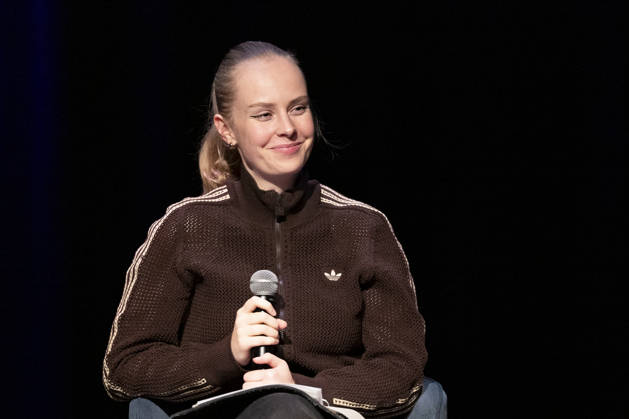 Poetry artist and author Clara LOESEL LÖSEL, smiling during her reading—a preview event for her new book, *Ich dachte, sowas fühle nur ich*—seated with a microphone; single frame, single photo, at the Theater am Tanzbrunnen, Cologne, on October 23, 2026