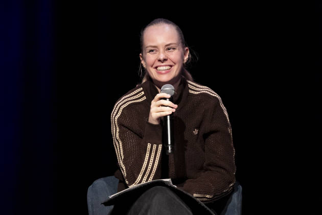 Poetry artist and author Clara LOESEL LÖSEL smiling, laughing, during her reading—a preview event for her new book, *Ich dachte, sowas fühle nur ich*—seated, holding a microphone; single frame, single photo, at the Theater am Tanzbrunnen, Cologne, on October 23, 2026