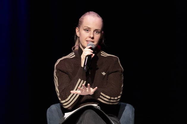Poetry artist and author Clara LOESEL LÖSEL, looking serious and focused, making a gesture with her hand during her reading—a preview event for her new book, *Ich dachte, sowas fühle nur ich*—seated with a microphone; single frame, single photo, at the Theater am Tanzbrunnen, Cologne, on October 23, 2026