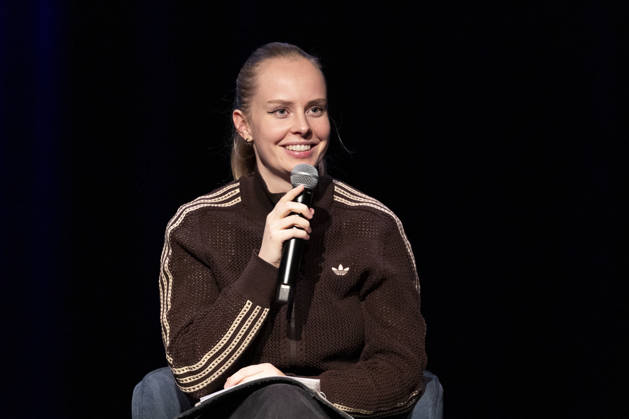 Poetry artist and author Clara LOESEL LÖSEL laughing during her reading, a preview show for her new book *Ich dachte, sowas fühle nur ich* (I Thought I Was the Only One Who Felt That Way), seated with a microphone; single frame, single photo, at the Theater am Tanzbrunnen, Cologne, on October 23, 2026