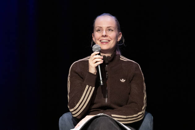 Poetry artist and author Clara LOESEL LÖSEL laughing during her reading, a preview show for her new book *Ich dachte, sowas fühle nur ich* (I Thought I Was the Only One Who Felt That Way), seated with a microphone; single frame, single photo, at the Theater am Tanzbrunnen, Cologne, on October 23, 2026