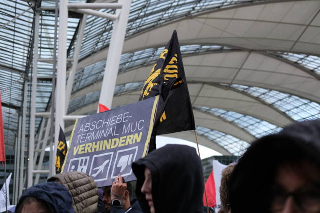 Protest at Munich Airport against planned deportation terminal MUNICH, GERMANY - OCTOBER 24: A protester holds a sign reading Abschiebeterminal MUC verhindern (Stop the MUC Deportation Terminal) as demonstrators with black flags gather inside the MAC Forum at Munich Airport in Munich, Germany on October 24, 2026. The campaign opposes plans to build a deportation terminal at Munich Airport operational from 2028. Merve Goettl Anadolu Munich Germany. Editorial use only. Please get in touch for any other usage.  Copyright: x2026xAnadoluxMervexGoettlx