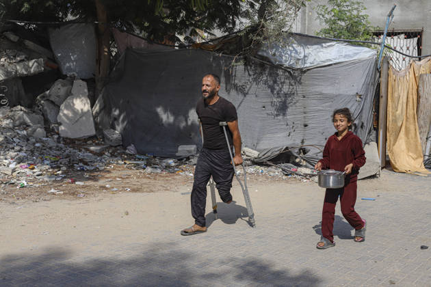 Gaza Palestinians Food Shortages 2026 A Palestinian man using crutches walks beside a young girl carrying a pot through a neighborhood of damaged buildings in Jabalia Refugee Camp, northern Gaza Strip, Palestine, on October 24, 2026. The UN says widespread damage, displacement and food shortages have left families across Gaza heavily dependent on humanitarian assistance, with food distributions reduced in October amid funding constraints. Jabalia Gaza Strip Palestinian Territories Copyright: xRamezxHabboubx