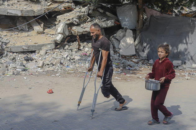 Gaza Palestinians Food Shortages 2026 A Palestinian man using crutches walks beside a young girl carrying a pot through a neighborhood of damaged buildings in Jabalia Refugee Camp, northern Gaza Strip, Palestine, on October 24, 2026. The UN says widespread damage, displacement and food shortages have left families across Gaza heavily dependent on humanitarian assistance, with food distributions reduced in October amid funding constraints. Jabalia Gaza Strip Palestinian Territories Copyright: xRamezxHabboubx