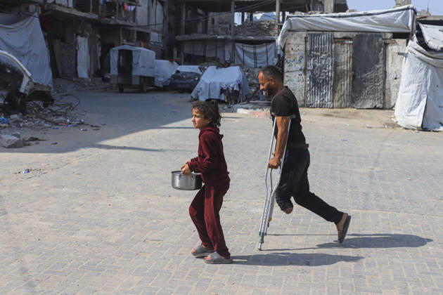 Gaza Palestinians Food Shortages 2026 A Palestinian man using crutches walks beside a young girl carrying a pot through a neighborhood of damaged buildings in Jabalia Refugee Camp, northern Gaza Strip, Palestine, on October 24, 2026. The UN says widespread damage, displacement and food shortages have left families across Gaza heavily dependent on humanitarian assistance, with food distributions reduced in October amid funding constraints. Jabalia Gaza Strip Palestinian Territories Copyright: xRamezxHabboubx
