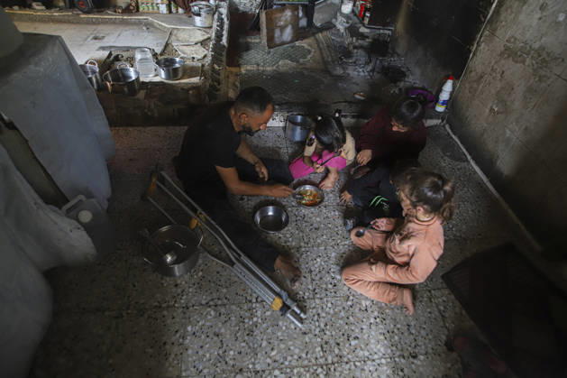 Gaza Palestinians Food Shortages 2026 A Palestinian man using crutches sits with children as they eat a meal received from a charity kitchen inside a damaged building in Jabalia Refugee Camp, northern Gaza Strip, Palestine, on October 24, 2026. The UN says widespread damage, displacement and food shortages have left families across Gaza heavily dependent on humanitarian assistance, with food distributions reduced in October amid funding constraints. Jabalia Gaza Strip Palestinian Territories Copyright: xRamezxHabboubx
