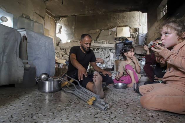 Gaza Palestinians Food Shortages 2026 A Palestinian man using crutches sits with children as they eat a meal received from a charity kitchen inside a damaged building in Jabalia Refugee Camp, northern Gaza Strip, Palestine, on October 24, 2026. The UN says widespread damage, displacement and food shortages have left families across Gaza heavily dependent on humanitarian assistance, with food distributions reduced in October amid funding constraints. Jabalia Gaza Strip Palestinian Territories Copyright: xRamezxHabboubx