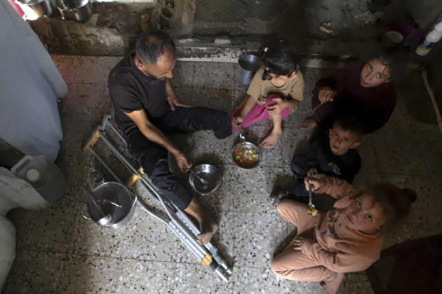 Gaza Palestinians Food Shortages 2026 A Palestinian man using crutches sits with children as they eat a meal received from a charity kitchen inside a damaged building in Jabalia Refugee Camp, northern Gaza Strip, Palestine, on October 24, 2026. The UN says widespread damage, displacement and food shortages have left families across Gaza heavily dependent on humanitarian assistance, with food distributions reduced in October amid funding constraints. Jabalia Gaza Strip Palestinian Territories Copyright: xRamezxHabboubx