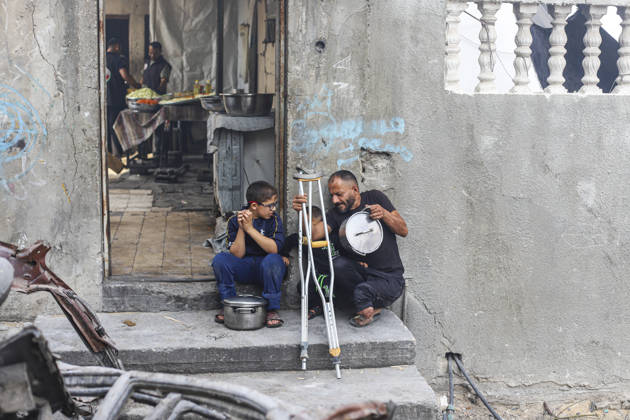 Gaza Palestinians Food Shortages 2026 A Palestinian man using crutches sits outside a damaged home beside children and cooking pots in Jabalia Refugee Camp, northern Gaza Strip, Palestine, on October 24, 2026. The UN says widespread damage, displacement and food shortages have left families across Gaza heavily dependent on humanitarian assistance, with food distributions reduced in October amid funding constraints. Jabalia Gaza Strip Palestinian Territories Copyright: xRamezxHabboubx