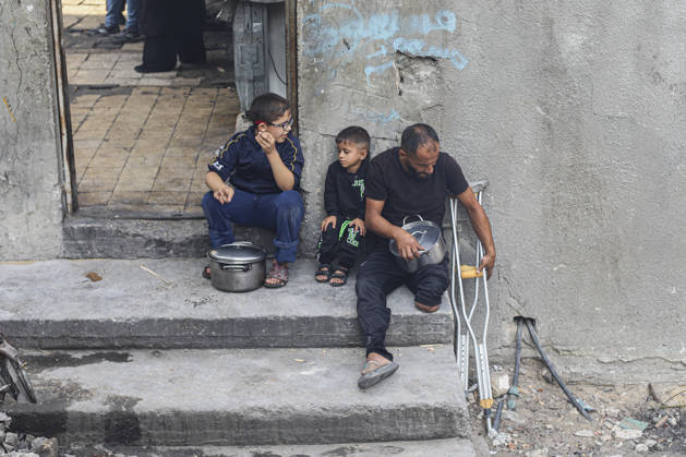 Gaza Palestinians Food Shortages 2026 A Palestinian man using crutches sits outside a damaged home beside children and cooking pots in Jabalia Refugee Camp, northern Gaza Strip, Palestine, on October 24, 2026. The UN says widespread damage, displacement and food shortages have left families across Gaza heavily dependent on humanitarian assistance, with food distributions reduced in October amid funding constraints. Jabalia Gaza Strip Palestinian Territories Copyright: xRamezxHabboubx
