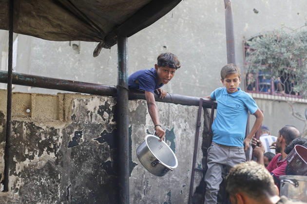 Gaza Palestinians Food Shortages 2026 A Palestinian boy carrying a cooking pot leans over a barrier beside a crowded food distribution point in Jabalia Refugee Camp, northern Gaza Strip, Palestine, on October 24, 2026. Community kitchens remain a key source of food in Gaza, where UN humanitarian agencies reported cuts to cooked-meal distributions in October because of funding shortages. Jabalia Gaza Strip Palestinian Territories Copyright: xRamezxHabboubx