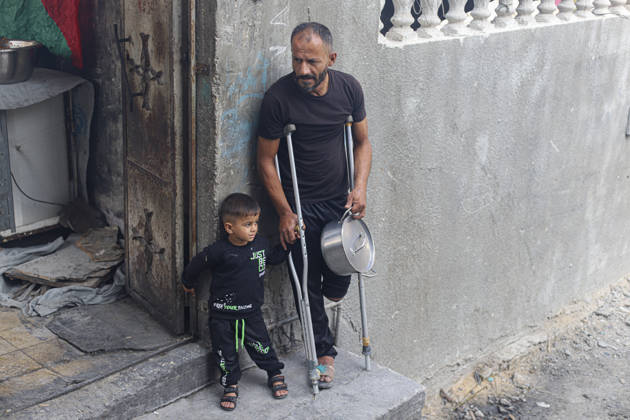 Gaza Palestinians Food Shortages 2026 A Palestinian man using crutches stands with a young child outside a damaged building while holding a metal cooking pot in Jabalia Refugee Camp, northern Gaza Strip, Palestine, on October 24, 2026. The UN says widespread damage, displacement and food shortages have left families across Gaza heavily dependent on humanitarian assistance, with food distributions reduced in October amid funding constraints. Jabalia Gaza Strip Palestinian Territories Copyright: xRamezxHabboubx