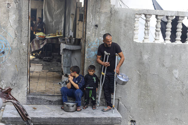 Gaza Palestinians Food Shortages 2026 A Palestinian man using crutches stands with children outside a damaged home, holding an empty cooking pot in Jabalia Refugee Camp, northern Gaza Strip, Palestine, on October 24, 2026. The UN says widespread damage, displacement and food shortages have left families across Gaza heavily dependent on humanitarian assistance, with food distributions reduced in October amid funding constraints. Jabalia Gaza Strip Palestinian Territories Copyright: xRamezxHabboubx