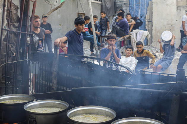 Gaza Palestinians Food Shortages 2026 Palestinians wait behind large cooking pots as food is prepared over an open flame at a charity kitchen in Jabalia Refugee Camp, northern Gaza Strip, Palestine, on October 24, 2026. Community kitchens remain a key source of food in Gaza, where UN humanitarian agencies reported cuts to cooked-meal distributions in October because of funding shortages. Jabalia Gaza Strip Palestinian Territories Copyright: xRamezxHabboubx