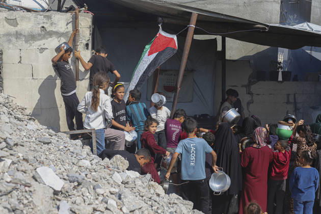 Gaza Palestinians Food Shortages 2026 Palestinians, including children, queue with cooking pots at a charity kitchen beside heavily damaged buildings, as a Palestinian flag is raised nearby in Jabalia Refugee Camp, northern Gaza Strip, Palestine, on October 24, 2026. Community kitchens remain a key source of food in Gaza, where UN humanitarian agencies reported cuts to cooked-meal distributions in October because of funding shortages. Jabalia Gaza Strip Palestinian Territories Copyright: xRamezxHabboubx