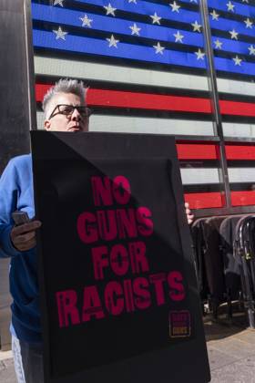 October 25, 2026, New York, New York, USA: A protester holds a sign that reads NO GUNS FOR RACISTS joining demonstrators with the anti-gun violence organization Gays Against Guns under the Times Square US Army Recruiting Station LED American flag to denounce U.S. Immigration and Customs Enforcement (ICE,) President Trump s immigrant detention and mass deportation policies, and to memorialize the people killed by Federal immigration agents. New York USA  - ZUMAr174 20261025_znp_r174_001 Copyright: xGinaxMxRandazzox