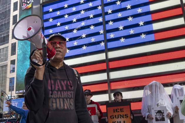 October 25, 2026, New York, New York, USA: JAY W. WALKER, President of Gays Against Guns leads chants at a demonstration under the Times Square US Army Recruiting Station LED American flag to denounce U.S. Immigration and Customs Enforcement (ICE) and President Trump s immigrant detention and mass deportation policies. People dressed in white shrouds are Human Beings, memorializing people killed by gun violence from Federal immigration agents by holding signs with their images and names. New York USA  - ZUMAr174 20261025_znp_r174_011 Copyright: xGinaxMxRandazzox